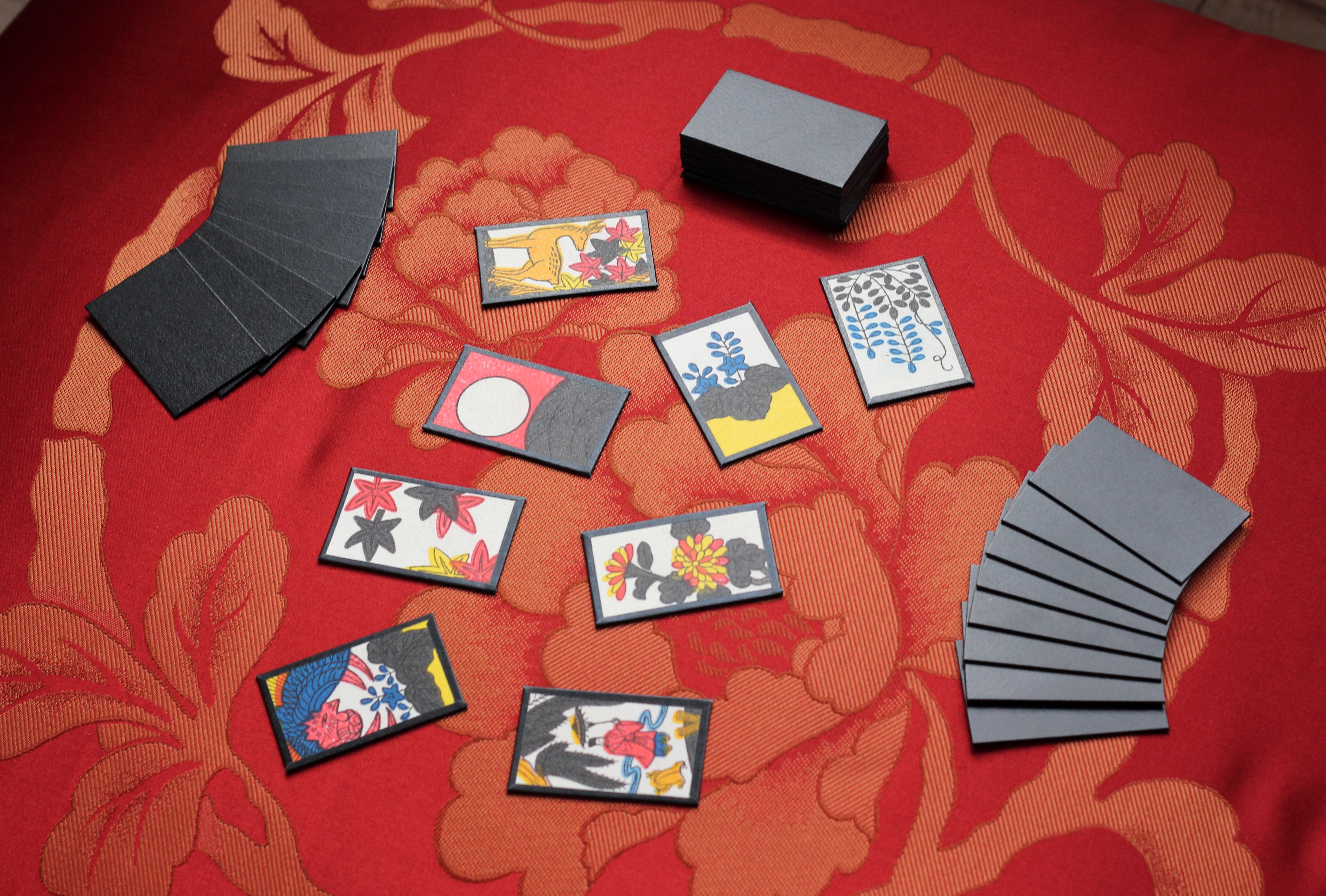 A typical setup of hanafuda cards for the game of koikoi, on top a red zabuton with a peony pattern. This set-up is called "te hachi ba hachi" - 8 cards in the hand, 8 cards in the field. The hanafuda pictured are homemade and based on a modified set of hanafuda graphics made by Louie Mantia, Jr.